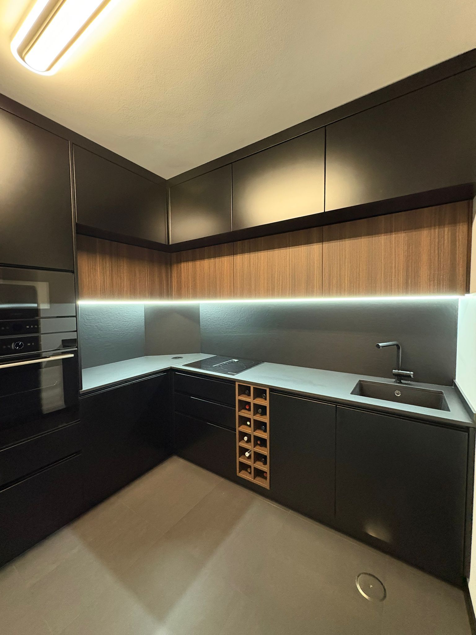 A mesma cozinha depois da remodelação, com móveis pretos mate, madeira e iluminação LED
